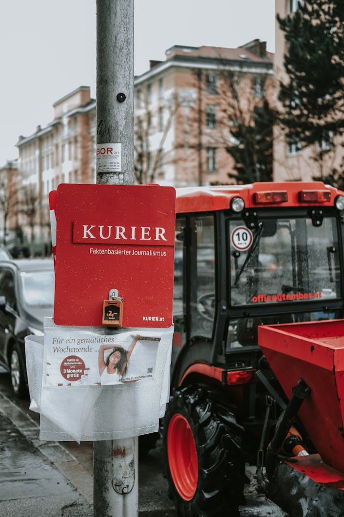 Street scene featuring a Kurier newspaper stand and a parked tractor on a cloudy day.
